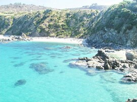 Un paisaje costero con aguas turquesas cristalinas, costas rocosas y colinas verdes al fondo.
