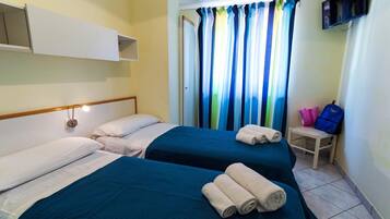 A hotel room with two beds, a TV mounted on the wall, and a window with colorful curtains.