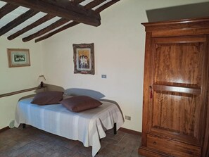 A bedroom with a bed, a wooden wardrobe, a framed picture on the wall, and a tiled floor. - Podere Il Caggio Appartements (San Gimignano)