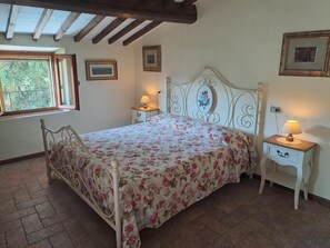 Un dormitorio con cama, dos mesitas de noche, una ventana y techo con vigas de madera.