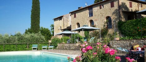 A pool area with a stone deck, lounge chairs, and a building with arched windows.