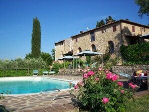 A pool area with a stone deck, lounge chairs, and a building with arched windows. - Podere Il Caggio Appartements (San Gimignano)