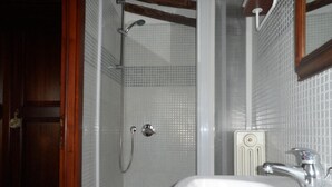 Een badkamer met een wit wastafelmeubel, een douche met een glazen deur, en een houten deurpost.
