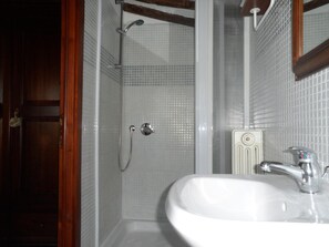 Un baño con lavamanos blanco, ducha con puerta de cristal y marco de puerta de madera.