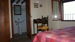 Ein Schlafzimmer mit einem Bett, einem Holzstuhl, einem Fenster und einem Badezimmer mit einem Waschbecken.