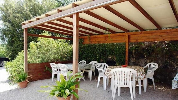 Eine überdachte Terrasse im Freien mit einer Holzhütte, weißen Plastikstühlen und einem Tisch.