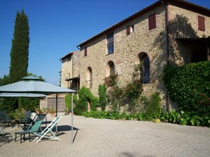 Un edificio de piedra con un patio cubierto, asientos al aire libre y abundante vegetación.