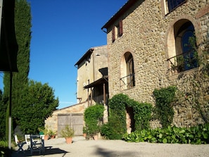 A stone building with arched windows and a covered porch. - Podere Il Caggio Appartements (San Gimignano)