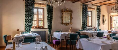 Ein Restaurant mit gedeckten Tischen, einem Chandelier und gemusterten Vorhängen.
