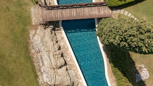 An aerial view of a swimming pool with a wooden bridge, surrounded by greenery and a rocky area. - Castello di Tornano (Gaiole in Chianti)