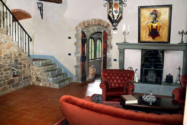 Una habitación con chimenea, un sillón rojo, una escalera y un cuadro en la pared.