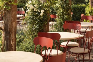 Outdoor seating with round tables and red chairs, surrounded by greenery and trees. - Castello di Tornano (Gaiole in Chianti)