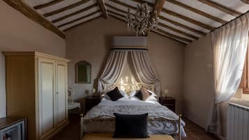 A bedroom with a canopy bed, wooden beams, a chandelier, a wardrobe, and a bedside table.