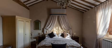 A bedroom with a canopy bed, wooden beams, a chandelier, a wardrobe, and a bedside table.