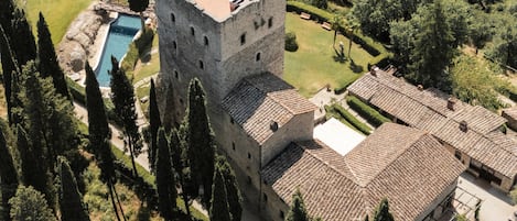 A historic stone building with a tower, a swimming pool, and a well-maintained garden.
