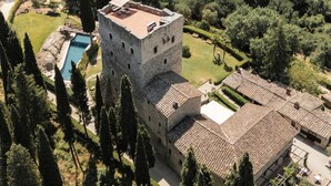 Un edificio histórico de piedra con una torre, piscina y un jardín bien cuidado.