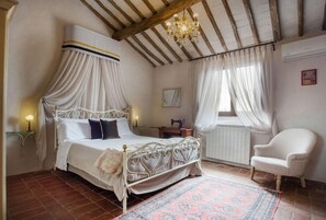 Un dormitorio con cama con dosel, candelabro, una silla y un radiador.