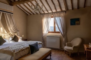 A bedroom with a bed, a chair, a radiator, and a window with curtains. - Castello di Tornano (Gaiole in Chianti)