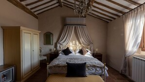 Un dormitorio con cama a dosel, vigas de madera, una araña y un armario, además de una mesita de noche.
