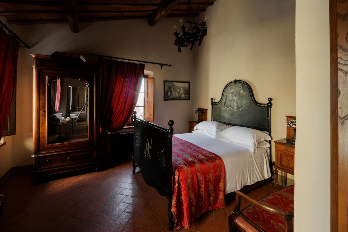 A bedroom with a wooden bed, a wooden wardrobe, a red chair, and a wooden floor.