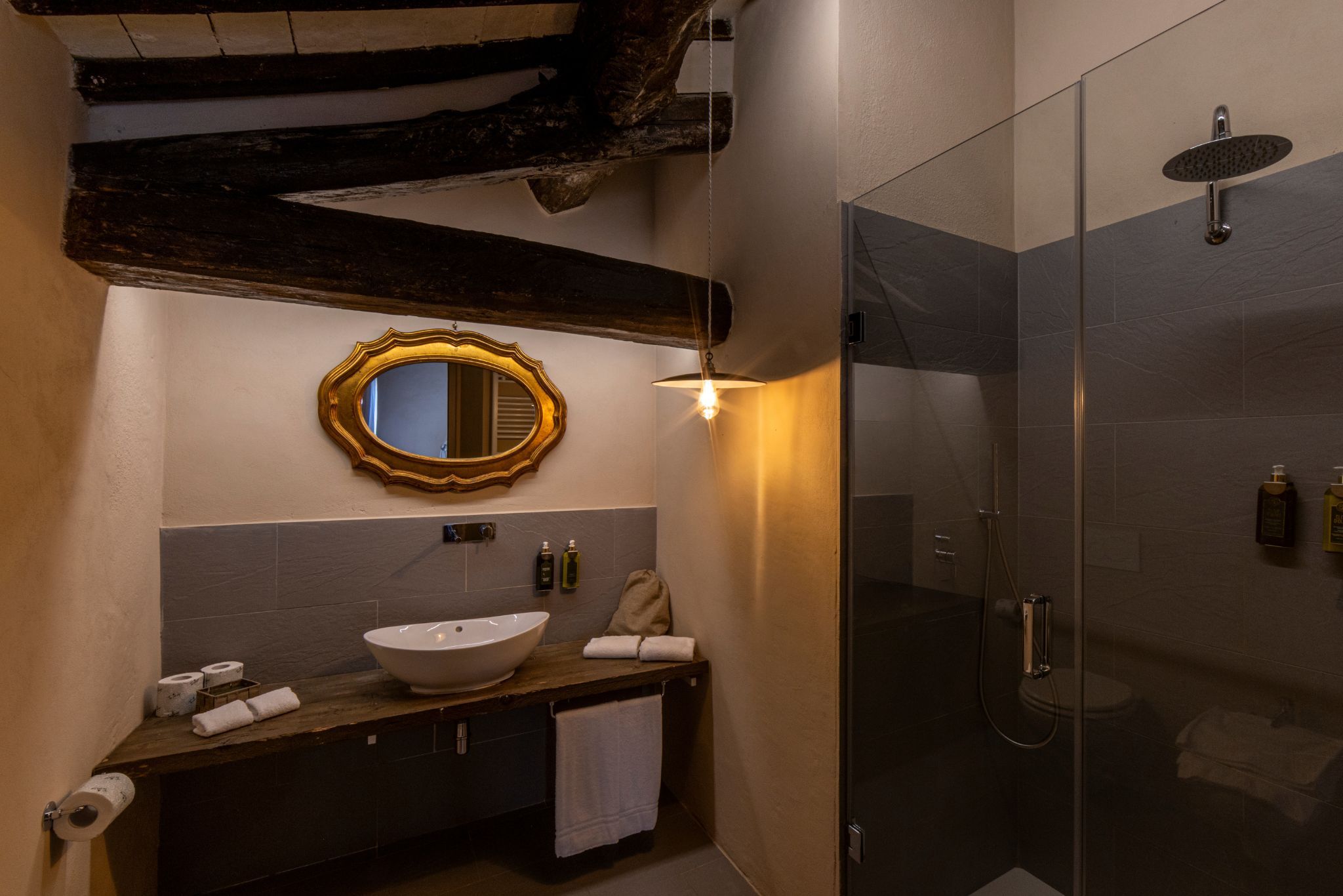Een badkamer met een houten wastafelmeubel, een grote spiegel, een rond wastafel en een douche met glazen wanden.
