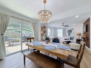 Ein geräumiger Wohnbereich mit Esstisch, Sofas, Deckenventilator und Blick auf den Garten.