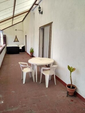 A covered outdoor area with a round table and chairs, a potted plant, and a door.