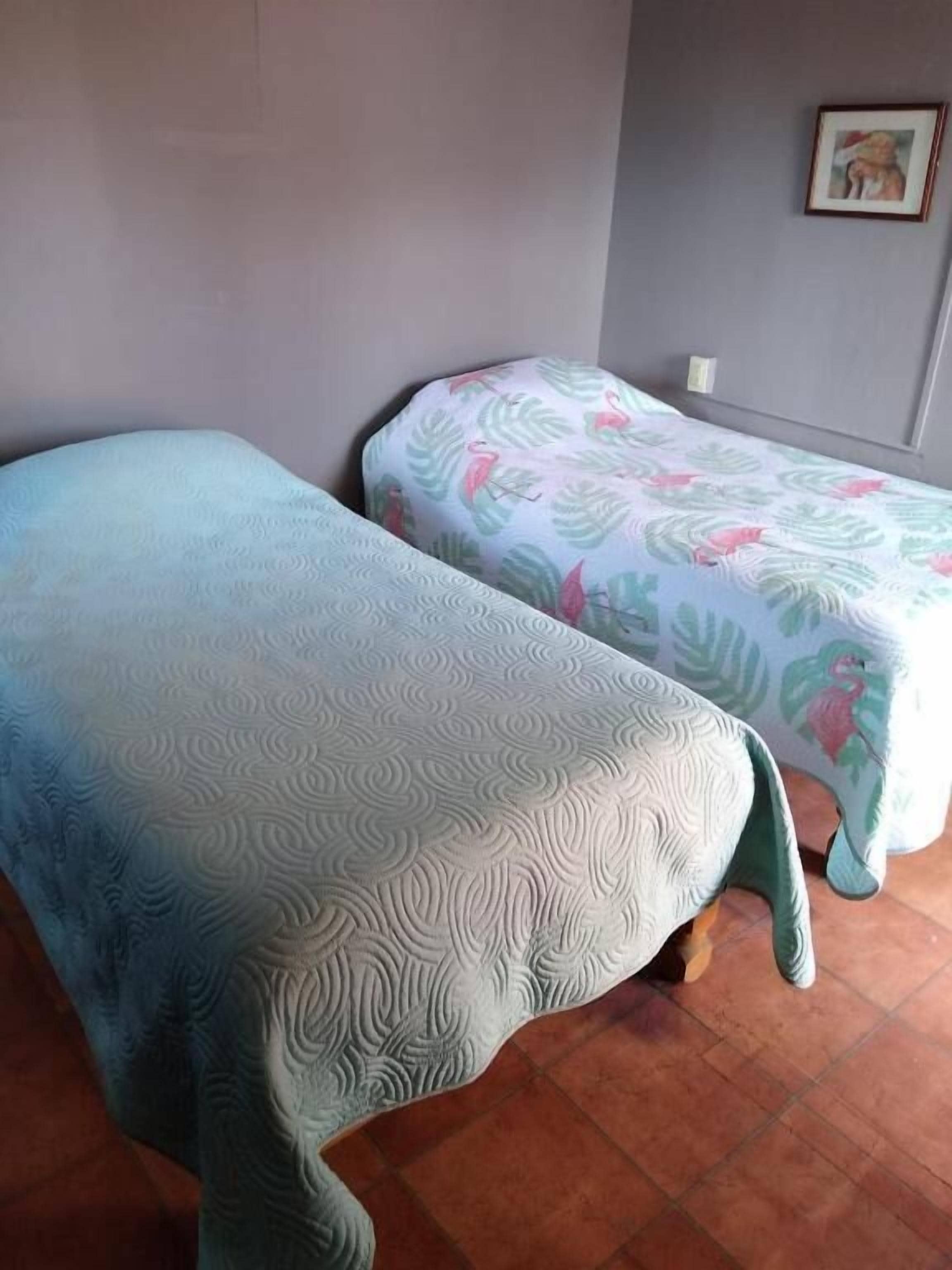 Two beds with patterned bedspreads in a room with tiled flooring and a plain wall.