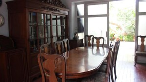 Un comedor con una mesa y sillas de madera, un aparador con puerta de vidrio y un ventanal con vistas a zonas verdes.