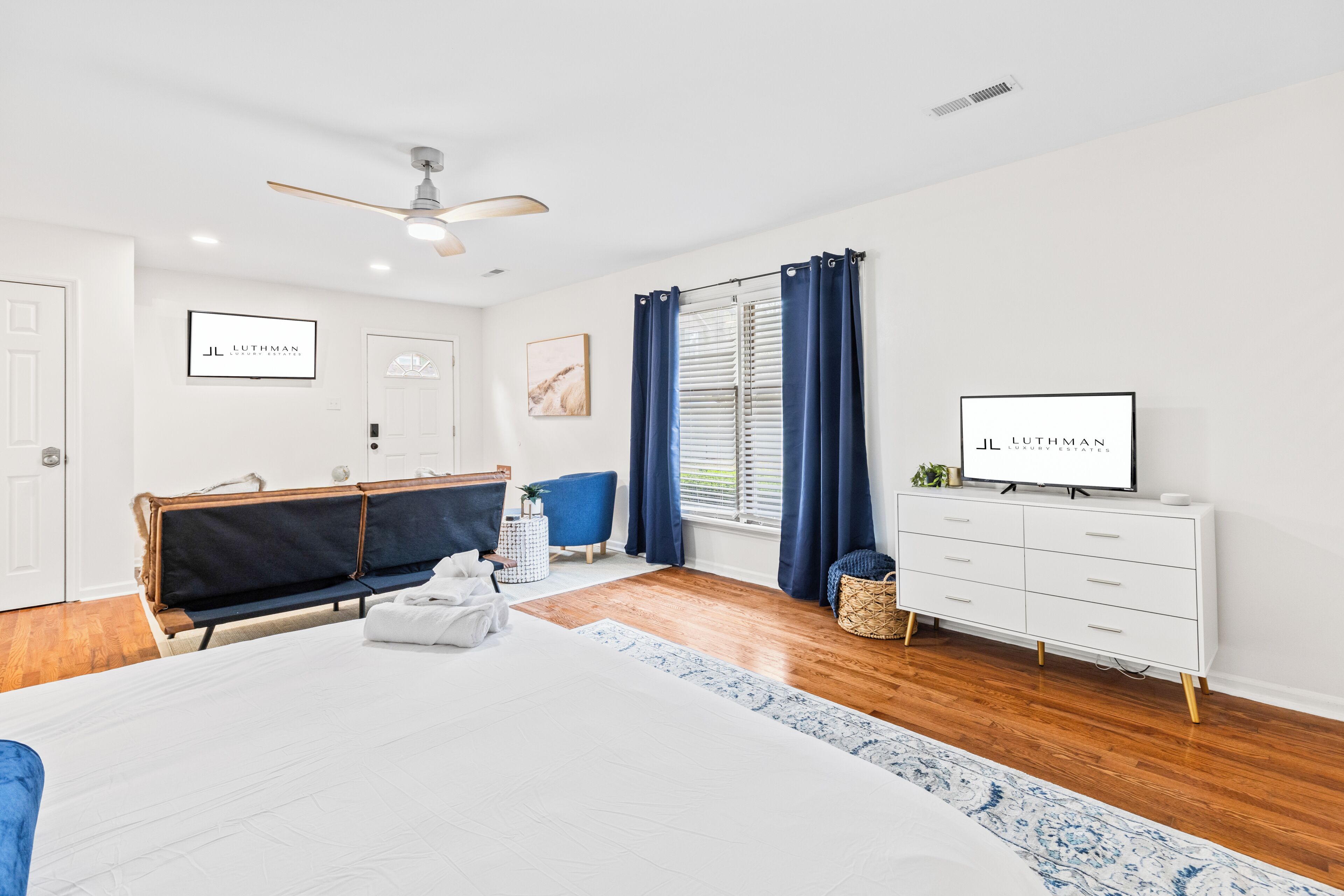 A modern hotel room with a bed, a vanity, a television, and a window with curtains.