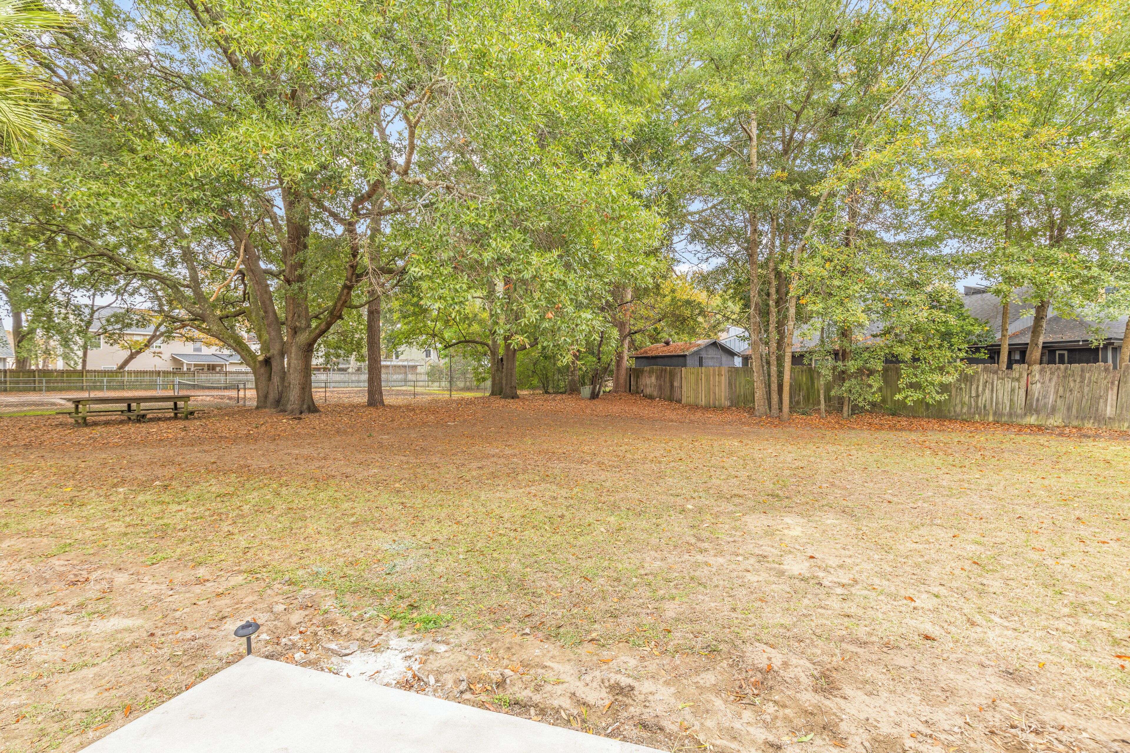 A fenced yard with trees, a picnic table, and a wooden fence.