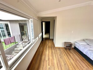 Een slaapkamer met een houten vloer, een bed, een klein nachtkastje en een raam met uitzicht.