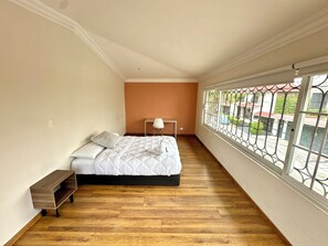 Een slaapkamer met een bed, nachtkastje en uitzicht door een raam.