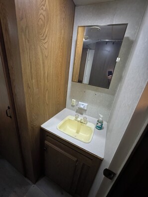 A bathroom with a wooden door, a white sink with a mirror above it, and a small bottle of hand soap on the counter.