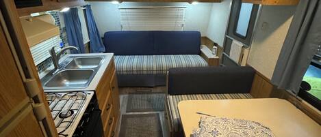 A compact RV interior with a kitchenette, a dining area, and a sleeping space.