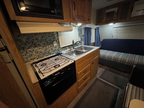 A compact kitchen with a gas stove, sink, and wooden cabinets.
