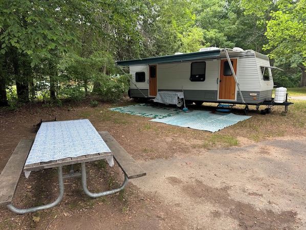 A recreational vehicle (RV) parked in a wooded area with a picnic table nearby.