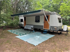 A stationary RV with a covered porch, a table, and a blue mat on the ground.