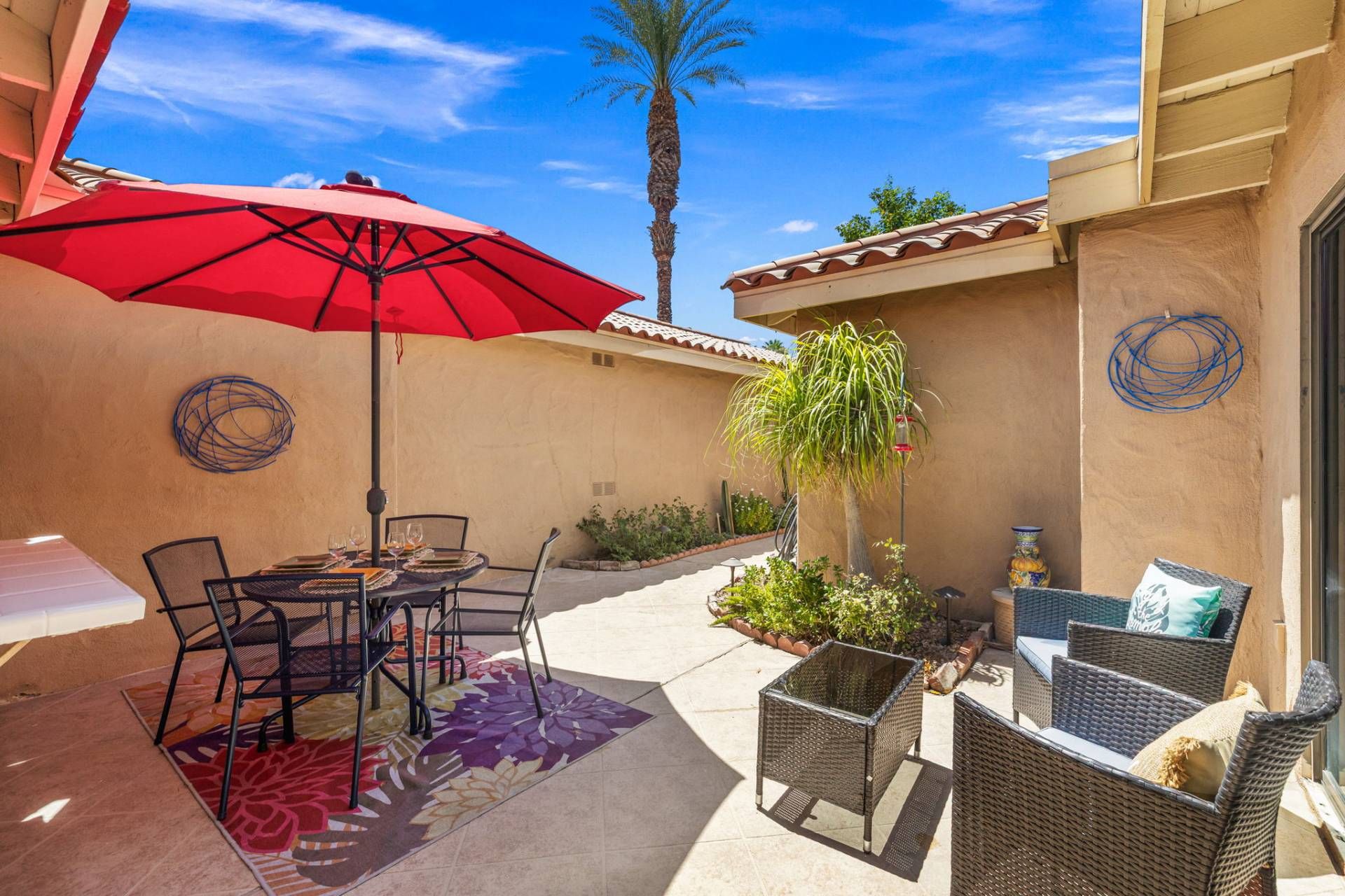 Une terrasse avec des meubles d’extérieur, un parasol rouge et une plante en pot.