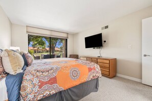 Ein Schlafzimmer mit Bett, Schminktisch, Fernseher und einer Schiebetür zum Patio.