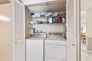 Une buanderie équipée de deux machines à laver, d’un sèche-linge et d’étagères remplies de divers objets.
