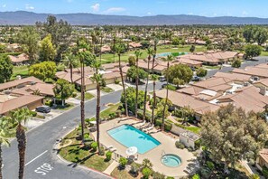 A residential area with a swimming pool, houses with red-tiled roofs, and palm trees. - Monterey Country Club Condo with Golf Course and Mountain Views, Pools, Spa and Private Patios (Palm Desert)