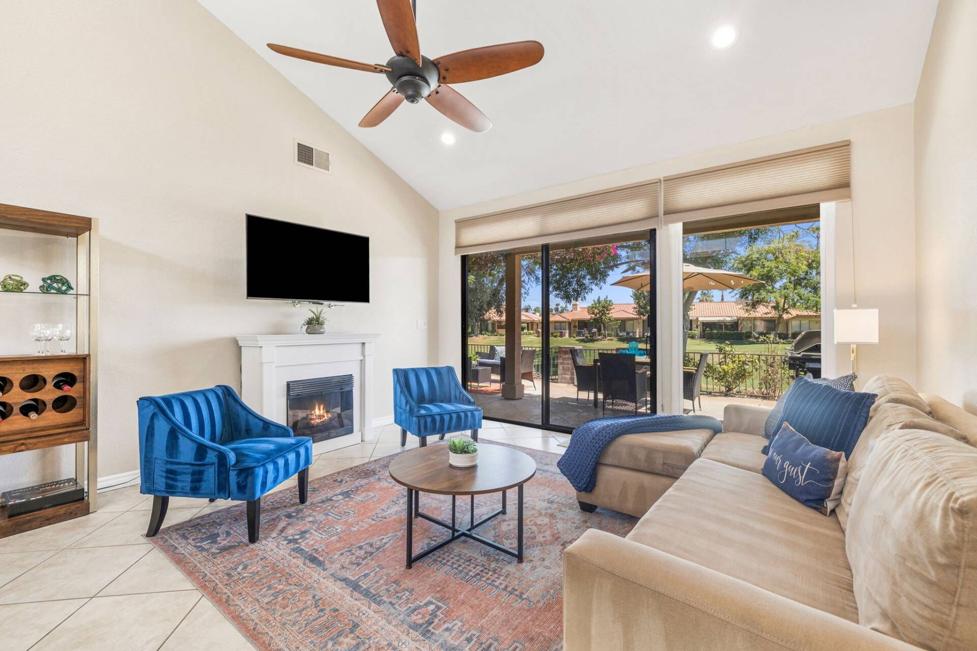 A living room with a fireplace, a ceiling fan, a TV mounted above it, and a large sliding glass door leading to an outdoor patio.