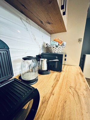 Eine Küche mit Holzarbeitsplatte, einem Wasserkocher, einer Kaffeemaschine und einem Wäschekorb mit Handtüchern.