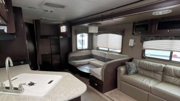 A compact RV interior with a kitchenette, a seating area, and a window for natural light. - Spacious   recreational vehicle in Cheyenne 2 bunks two sofa beds and one master (Cheyenne)