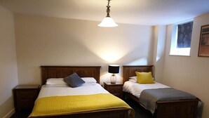 A bedroom with two wooden beds, a nightstand with a lamp, and a hanging light fixture.