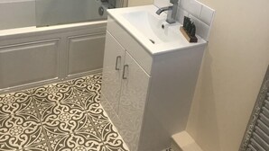 Een badkamer met een douche, een wastafel, een spiegel en vloertegels met een patroon.