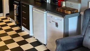 A compact kitchen with a black and white checkered floor, a refrigerator, a coffee maker, and a microwave.