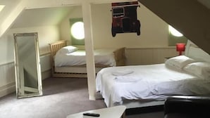 A bedroom with a lofted sleeping area, a bed, a small table, a couch, and a hanging artwork.