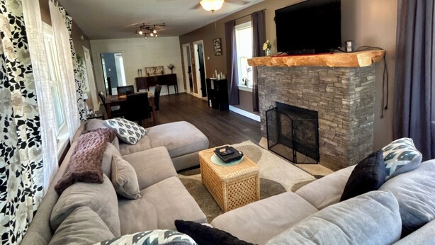 A living room with a large sofa, a fireplace, a television, and a dining area in the background.